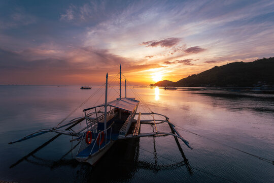 View of a boat reflecting the sunset colors on the water near the shore, Bais, Negros Oriental, Philippines.