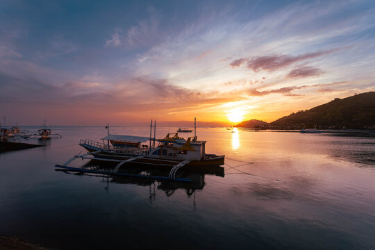 View of the tranquil bay reflecting the vibrant sunset hues, with boats gently resting on the calm water, Bais, Negros Oriental, Philippines.