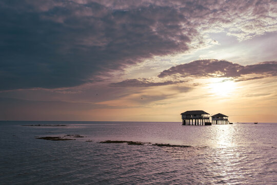 View of stilt houses standing resilient against the encroaching tide, silhouetted by the fiery kiss of the setting sun, Manjuyod, Negros Oriental, Philippines.