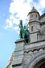Fototapeta premium Bronze lion statue on pedestal in front of monumental cathedral facade with arches and towers. Historic architecture and symbolic sculpture in urban heritage setting.
