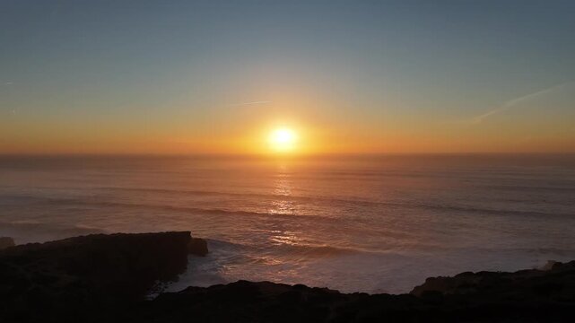 Atlantic sunset over ocean waves with sun half below horizon aerial drone shot