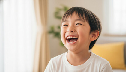 Naklejka premium Close up portrait of a happy young Asian boy laughing cheerfully in a bright cozy living room