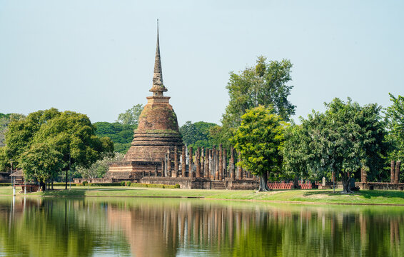 Ancient Buddhist stupa and ruins reflected in still water surrounded by trees