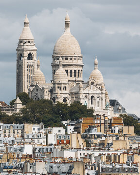 view of the Sacre-Coeur Basilica standing majestically above the rooftops, its pale stone contrasting with the darker hues of the surrounding buildings, Paris, France.