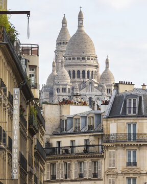 view of the Sacre-Coeur Basilica rising majestically beyond the rooftops of aged buildings, Paris, France.