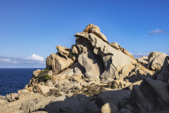 View of sun-drenched, sculpted granite boulders rise against the azure sky, meeting the deep blue sea in Capo Testa, Sardegna, Italy.