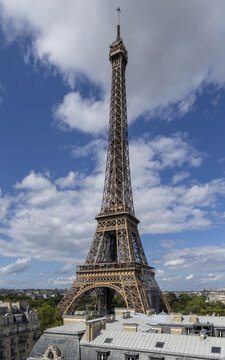 View of the iconic Eiffel Tower piercing the blue sky dotted with fluffy white clouds, standing tall above the city, Paris, Ile-de-France, France.