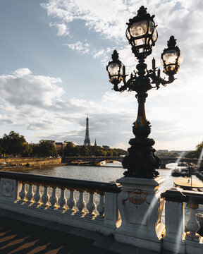View of the Eiffel Tower standing tall beyond the bridge and lamppost, with the river reflecting the sky's gradient, Paris, France.