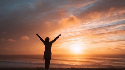 Fototapeta premium Silhouette of person standing with arms outstretched embracing a breathtaking sunset over ocean horizon