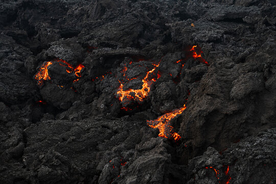View of molten lava flowing through jagged, black volcanic rock, a fiery spectacle of nature's raw power, Grindavik, Grindavikurbaer, Iceland.