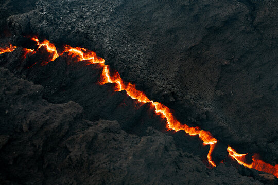 View of a fiery river of molten lava snakes through the dark, rugged landscape, a stark contrast of destruction and raw power, Grindavik, Iceland.