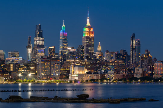 New York City skyscrapers illuminated with rainbow colors for LGBTQ+ Pride week. Evening view Midtown Manhattan across Hudson River