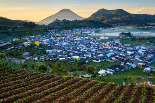 View of a town nestled in a valley with its colorful houses and lush green fields contrasting against the majestic mountain backdrop, Banjarnegara, Indonesia.