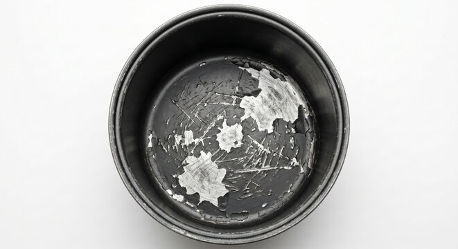 Top-down view of a ruined non-stick pot with severely scratched and peeling Teflon coating exposing bare metal.