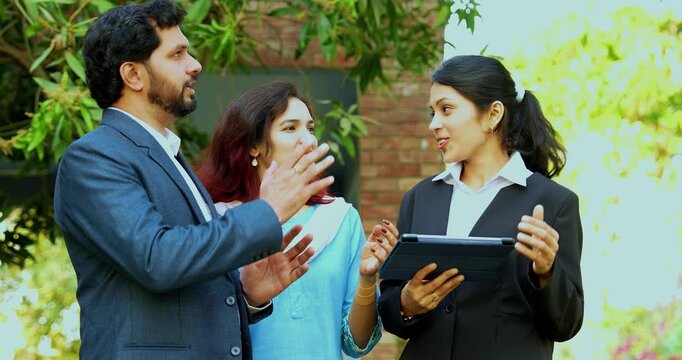 Indian woman real estate agent with young married couple walking in new property with laptop to review digital floor plans and architectural layouts during a professional home walkthrough