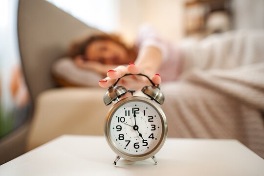 Woman hitting snooze button on alarm clock in morning