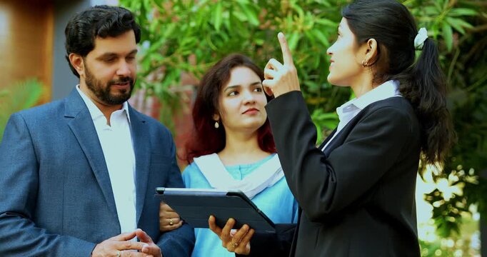 Indian woman event planner discussing with young couple outdoors in a lawn using a tablet computer to visualize the wedding or party layout during a successful professional consultation