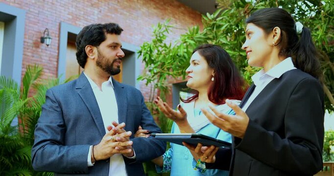 Indian woman event planner discussing with young couple outdoors in a lawn using a tablet computer to visualize the wedding or party layout during a successful professional consultation