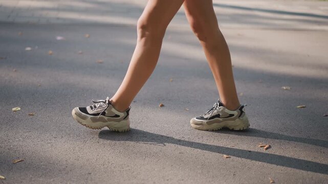 White woman walking on pavement in soft evening light, sneakers on asphalt, casual shorts and calm stride, solitude and wellness focus, following personal lifestyle decree for daily movement