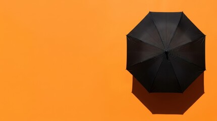 Top view of a classic black umbrella isolated on a vibrant orange surface with harsh shadow.
