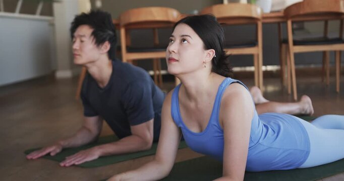 From forearms, Asian couple in studio, woman wearing tank lifting chests to extend spine on mats