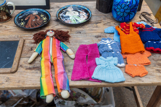 London, UK, December 2, 2025, A collection of vintage handmade dolls and knitted doll clothes displayed on a wooden table at an outdoor Spitalfields market.