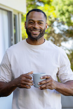 African American man standing and holding gray ribbed mug in light beige T-shirt on porch