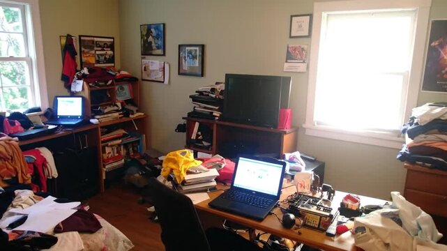 A cluttered bedroom with multiple laptops, clothes, and various items scattered around, creating a messy environment.