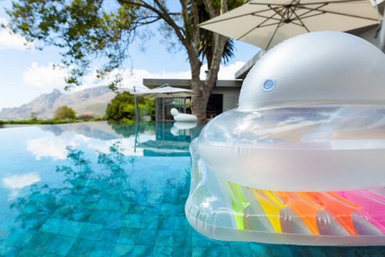 Translucent inflatable float floating on turquoise infinity pool, reflecting sky and palm trees
