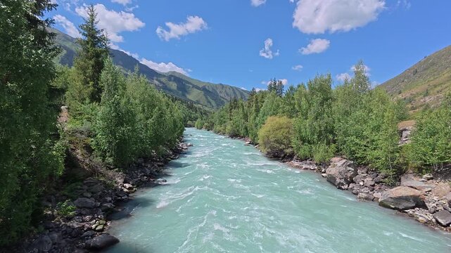 Koksu River flowing through a scenic mountain valley in Kazakhstan under bright blue sky with soft clouds. Turquoise water, rocky banks and dense green forest create a pristine natural landscape of Ce