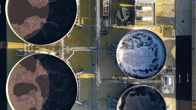 Aerial view of the circular tanks at Lenzing Fibers Grimsby, showcasing the dark, textured liquid contrasting with the light, foamy water, Grimsby, United Kingdom.