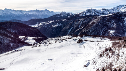 Obraz premium Aerial panorama of a snowy alpine valley with a small mountain village surrounded by dramatic peaks and winter landscapes