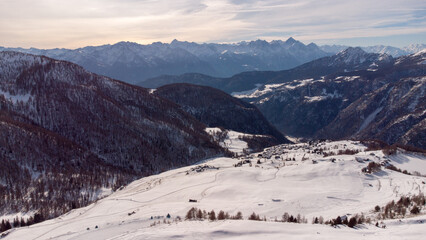 Aerial panorama of a snowy alpine valley with a small mountain village surrounded by dramatic peaks...