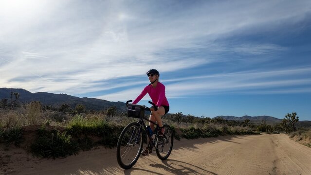 Woman rides a bike along a dirt path in Joshua Tree National Park under a blue sky with scattered clouds in California