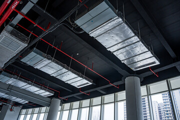 Naklejka premium Industrial-style office interior with exposed ceiling, ventilation ducts, and large windows overlooking the city