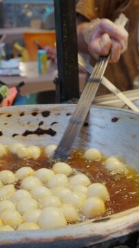 Street vendor frying round dough balls zalabia in hot oil inside metal pan. Vendor uses metal tongs to turn golden pieces of lugaimat while oil bubbles around them.Khan El Khalili bazaar, Cairo, Egypt