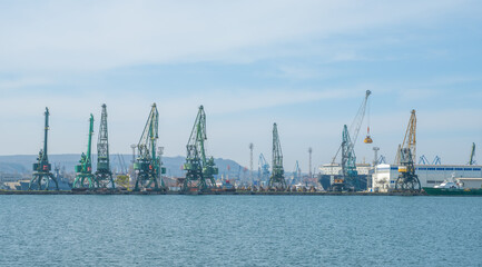 Obraz premium Industrial sea port panorama featuring rows of tall cargo cranes, docks, and ships under a clear sky. Busy maritime logistics and commercial shipping infrastructure