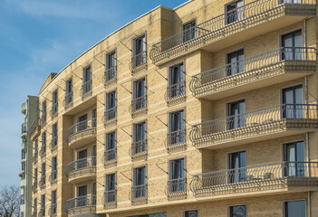 Fototapeta premium Modern yellow brick apartment building facade featuring numerous balconies with elegant wrought iron railings against a clear blue sky background in daylight