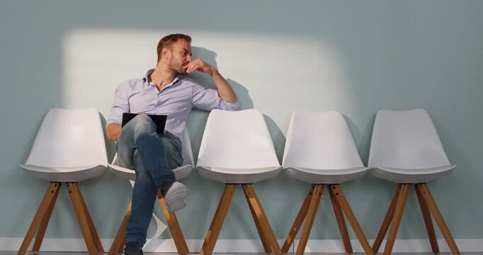 Man waiting for job interview in office. The candidate dozes on a chair with a clipboard, anxious about recruitment, while HR evaluation looms. Captures fatigue and patience in the hiring process.