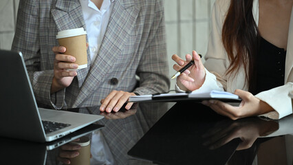 Two women are sitting at a table with a laptop and a cup of coffee