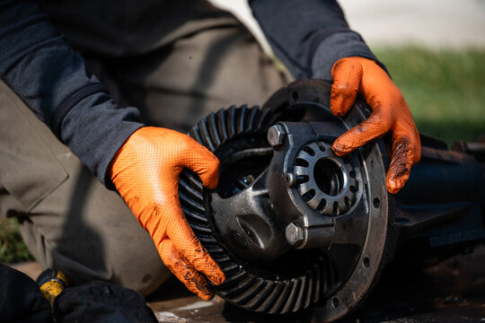 Mechanic repairing car differential gear assembly with gloved hands