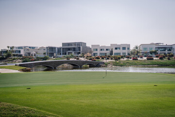 Golf course landscape featuring a green lawn, a small bridge, and modern residential buildings in the background