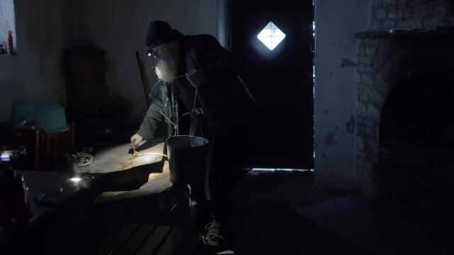 Elderly bearded monk in Mount Athos drawing water from an indoor well using a bucket and rope