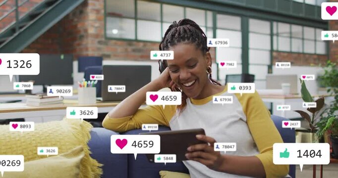 Woman tapping tablet on blue couch and generating heart icons and tracking marketing metrics