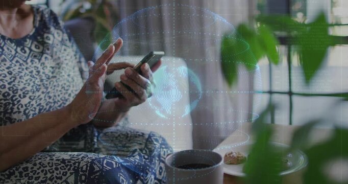 Senior woman tapping smartphone on sofa, tech holographic globe pulsing and revealing global data