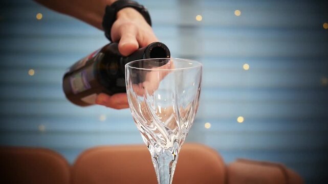 Close-up of a nice wineglass and a male hand pouring red wine from a bottle into it