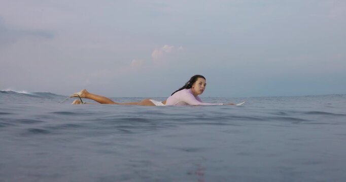 Young surfer woman rowing on surfboard in ocean.