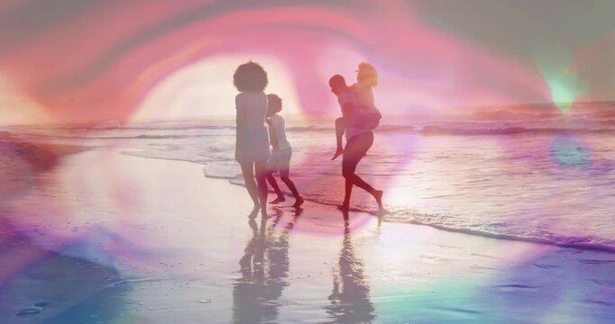 Family walking sunset shore travel woman reaching dad carrying child on back to join lens flares