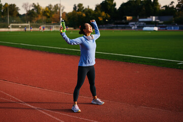 Asian woman celebrating successful workout on stadium running track