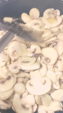 Video vertical de unos Champi&ntilde;ones blancos laminados cocin&aacute;ndose en sart&eacute;n y removidos con esp&aacute;tula